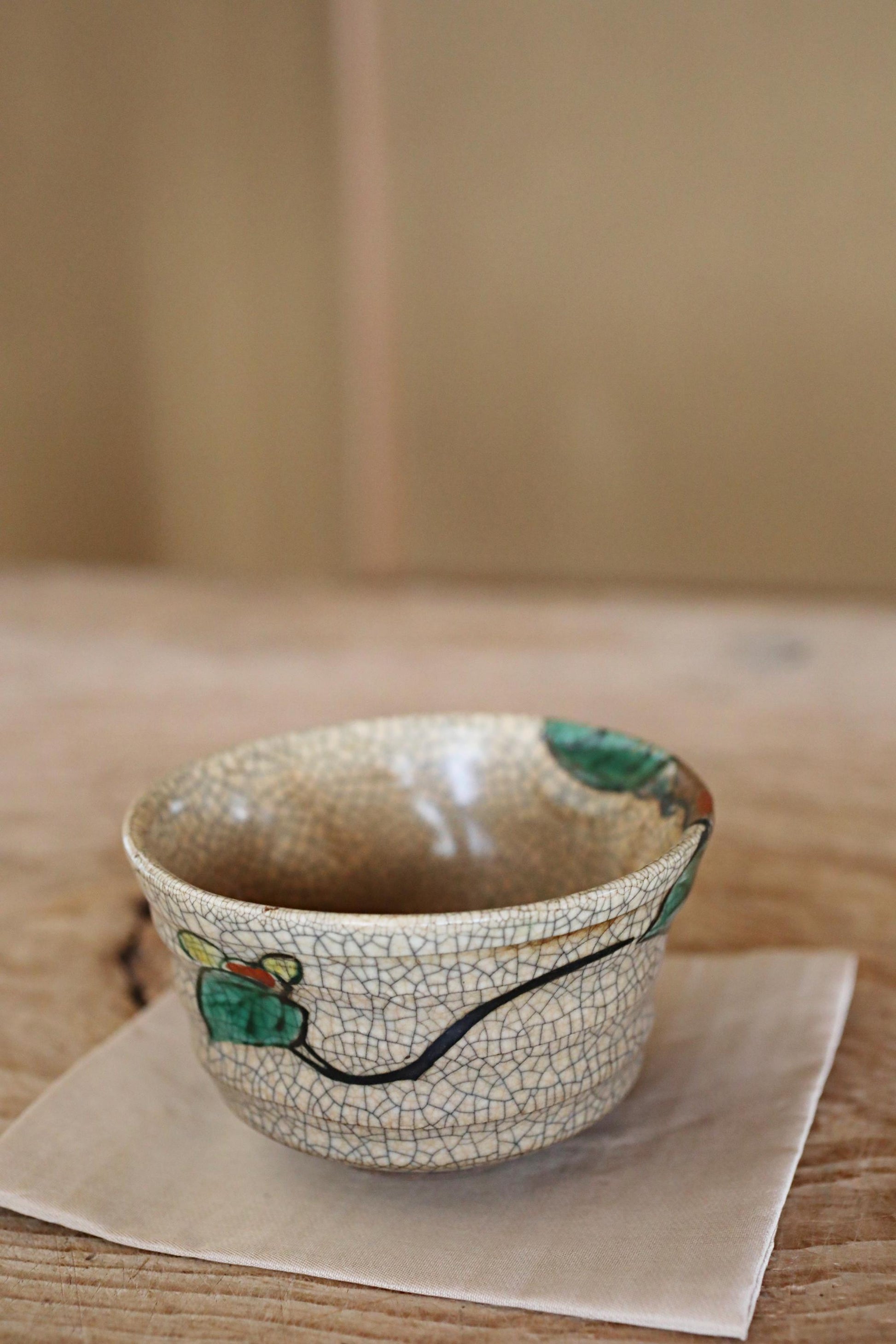 A ceramic bowl with a floral design sits on a beige napkin on a wooden table.