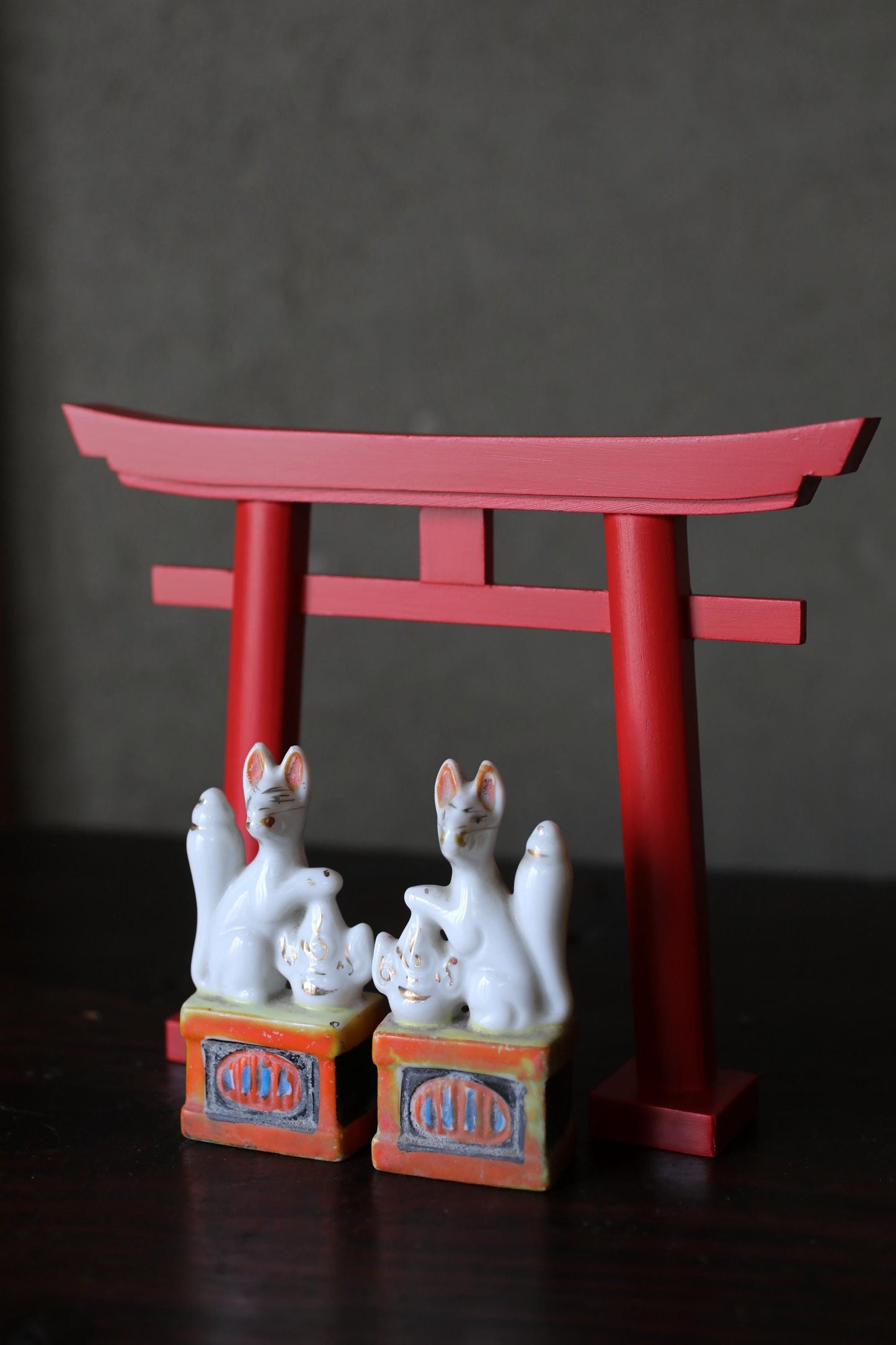 two ceramic figurines of cats sitting on a red torii gate, which is a traditional Japanese gate used as a symbol of the entrance to a shrine.
