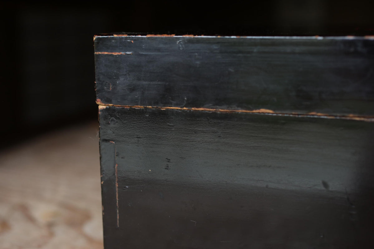 A close-up view of a black, weathered surface with visible signs of wear and tear, including peeling paint and a rough texture.