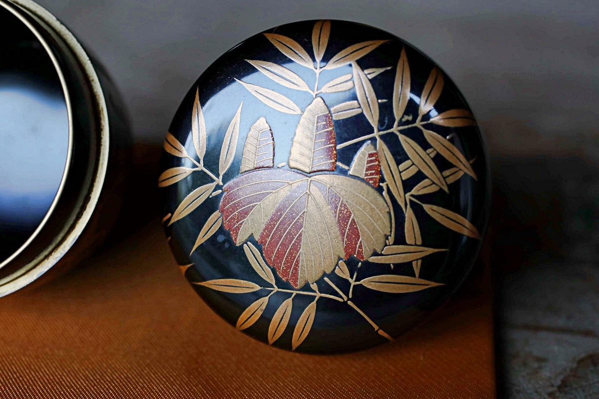 A decorative black and gold container with a floral design on it, placed on a wooden surface.