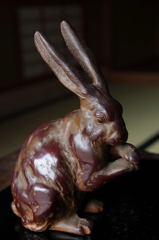 A brown, weathered metal rabbit figurine is sitting on a black surface.