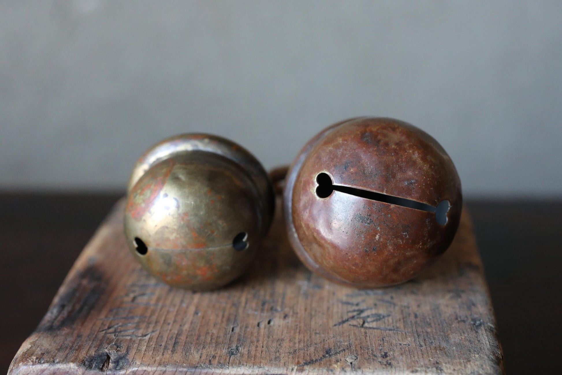 Two antique brass bells with holes on a wooden surface.