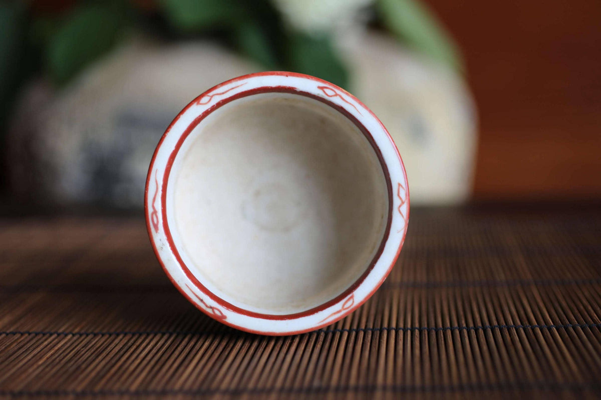A white ceramic bowl with a red border sits on a bamboo mat, with a blurred background.