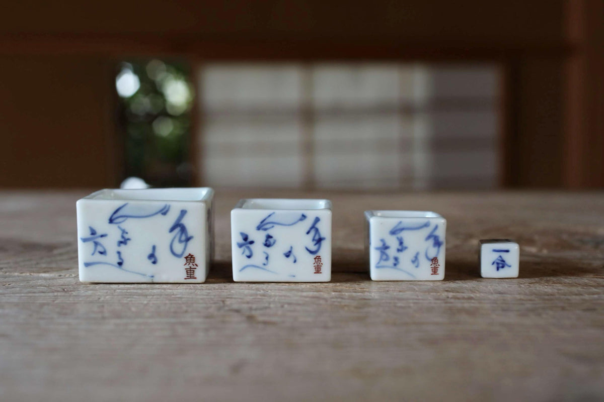 Three small white ceramic containers with blue designs and Chinese characters on them, arranged on a wooden surface.