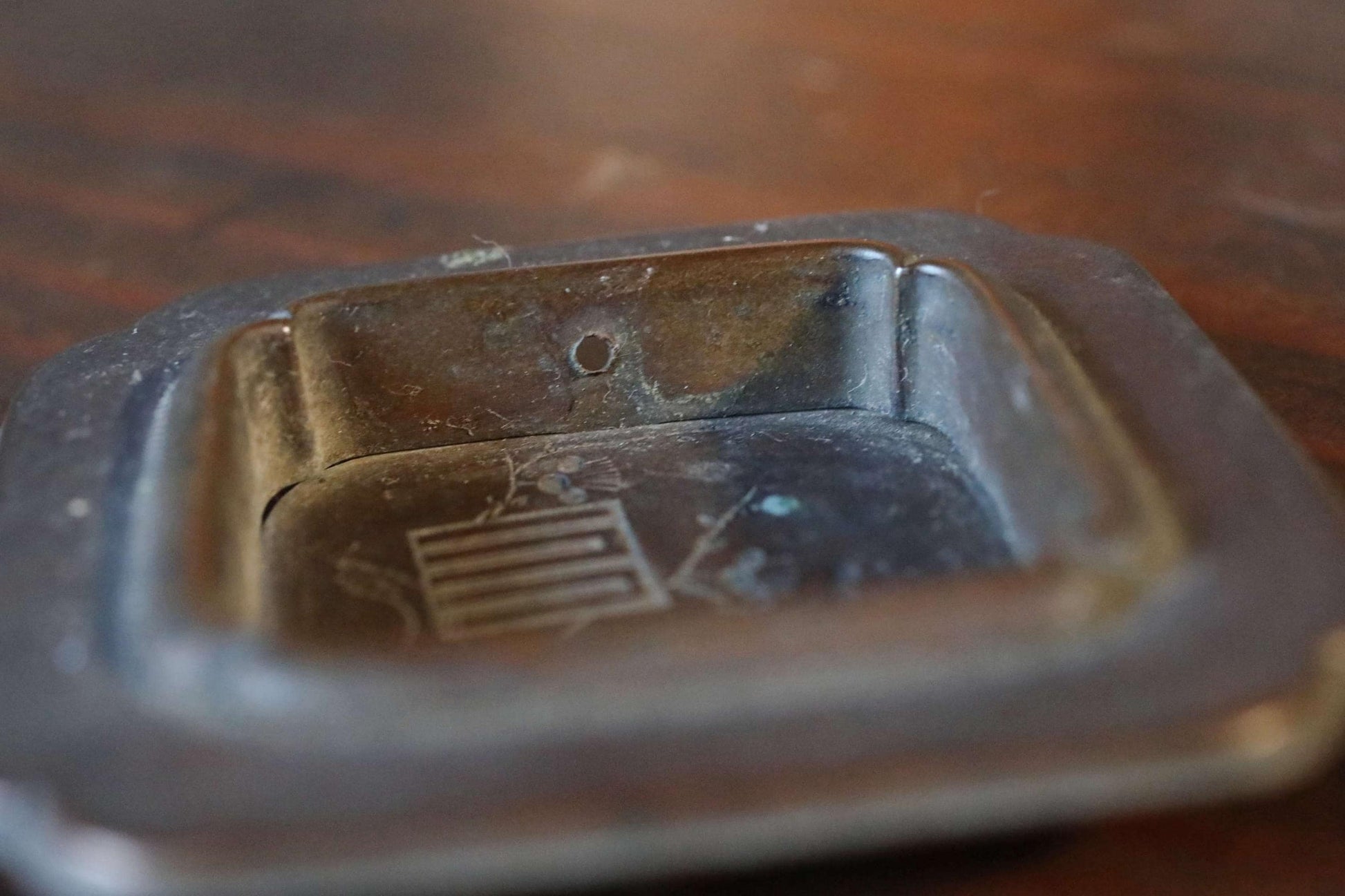 A close-up view of a metal ashtray on a wooden surface.