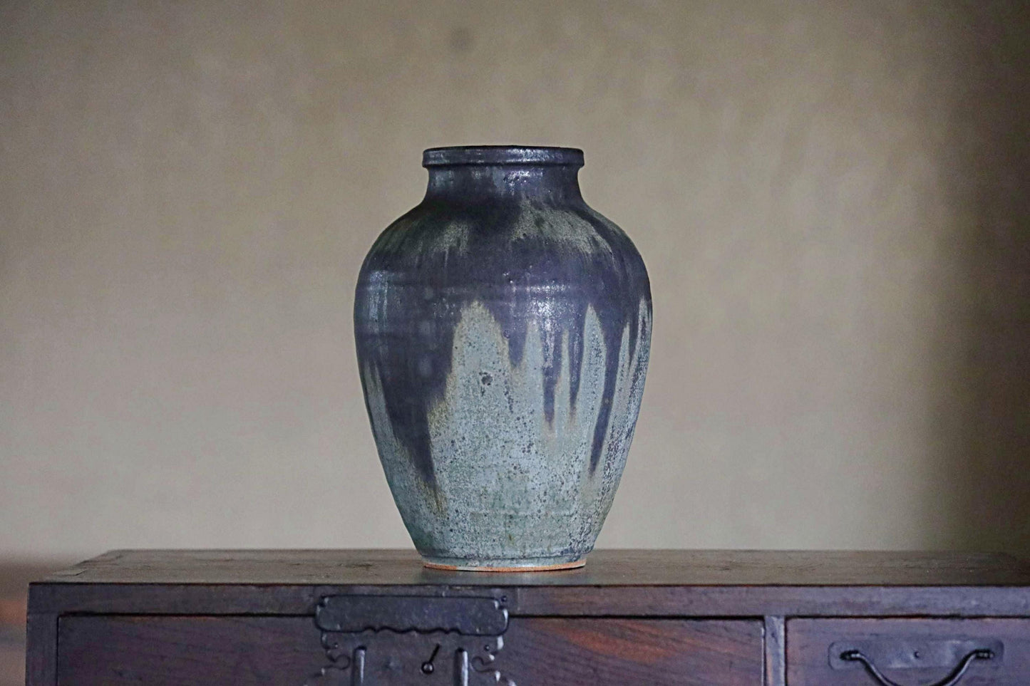 A dark blue ceramic vase with a textured surface sits on a wooden surface against a plain background.