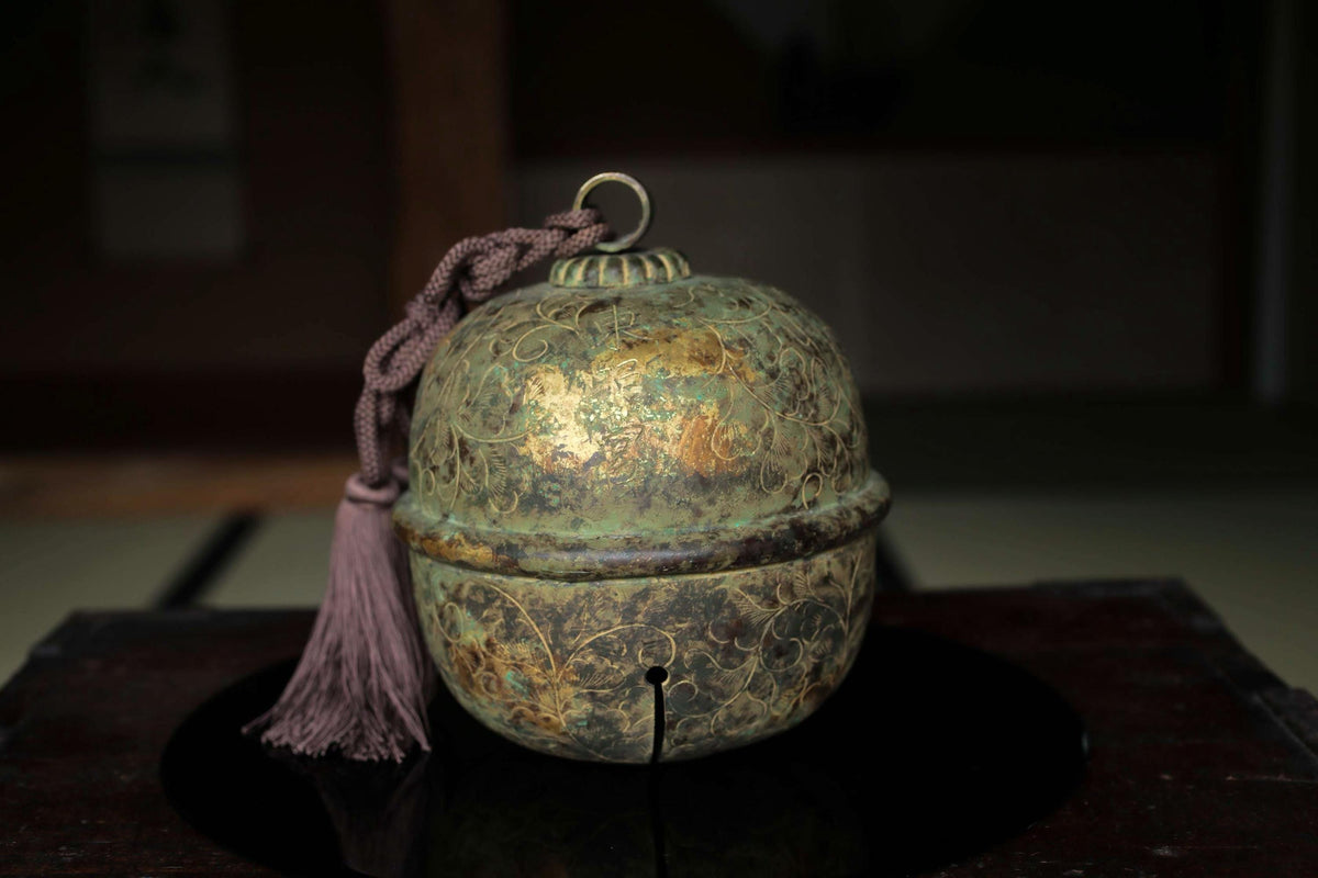 An ornate, antique-looking bell with a tassel hanging from the handle, sitting on a dark surface.