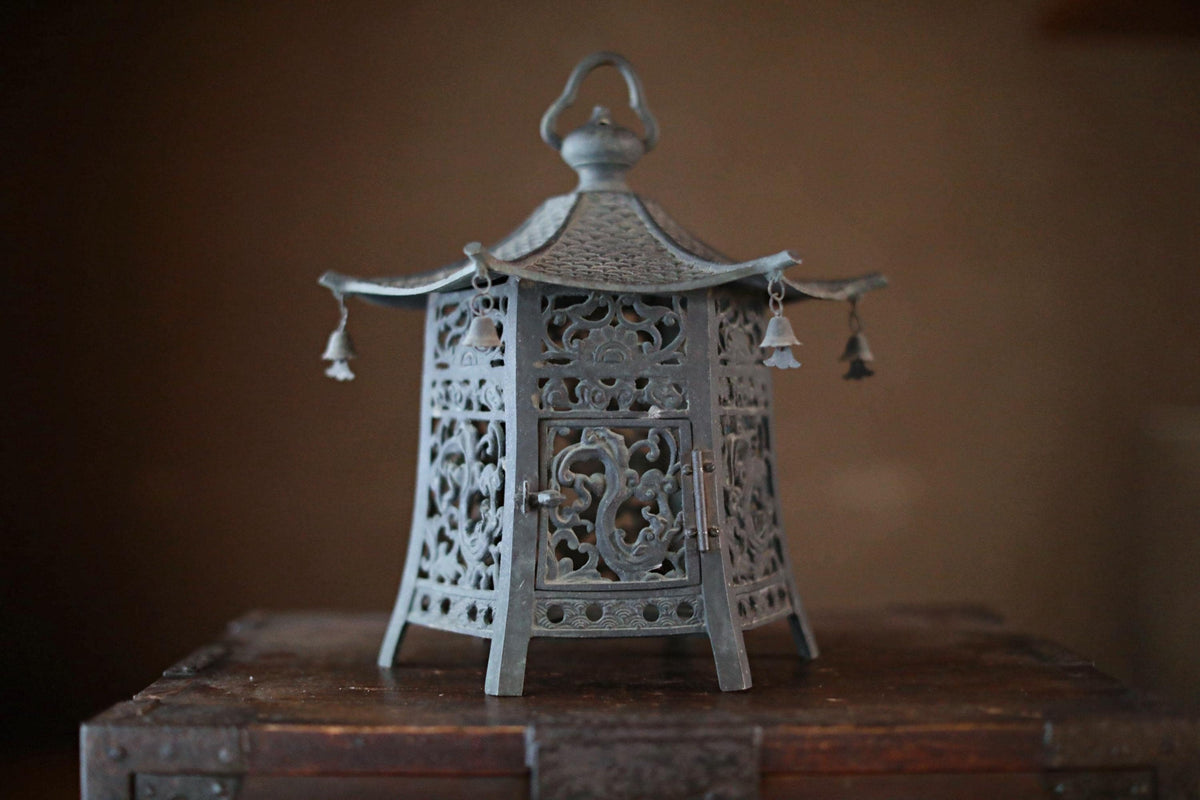 A decorative metal lantern with intricate designs and hanging bells, placed on a wooden surface.