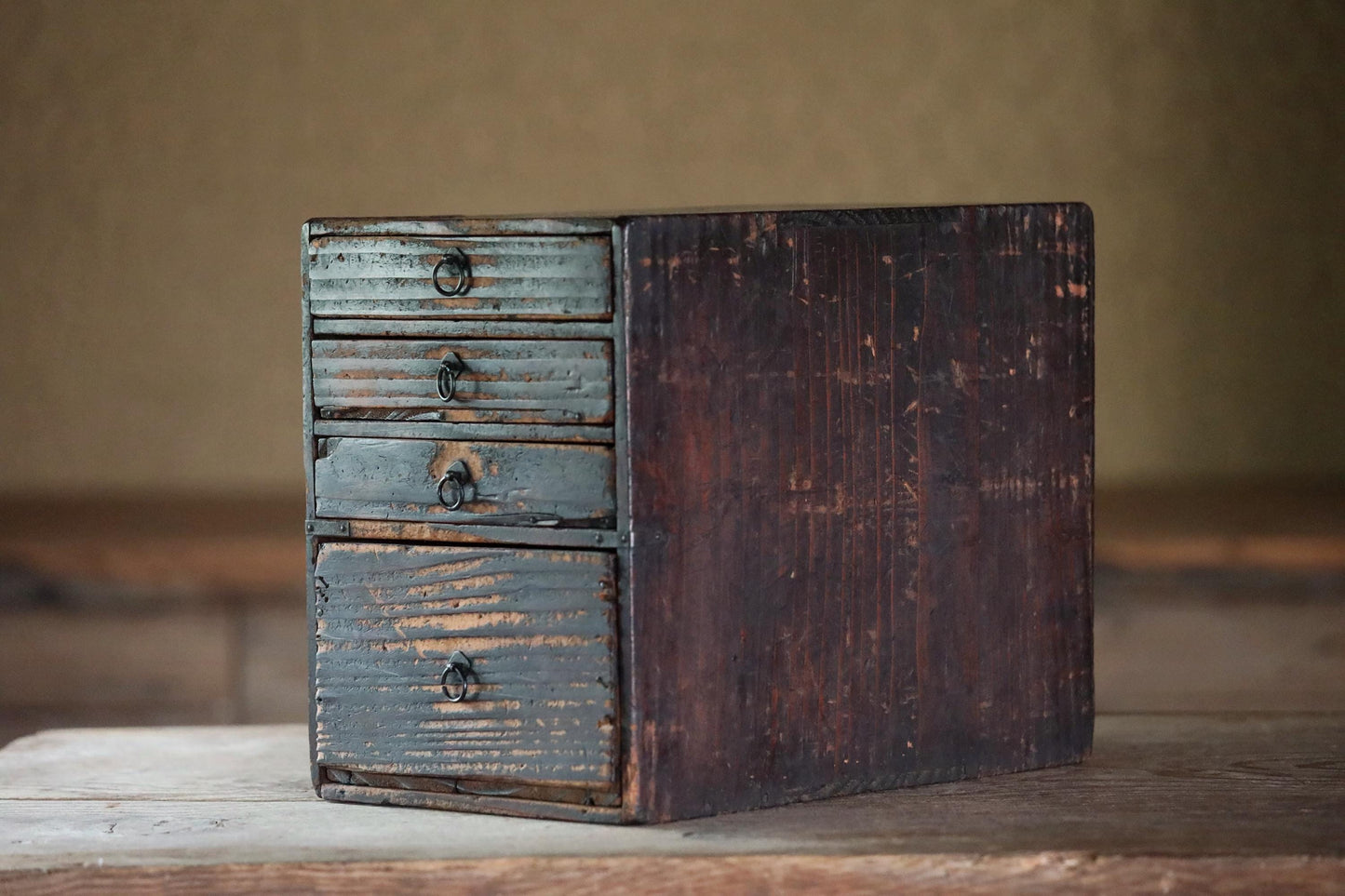 An old, weathered wooden drawer with four compartments sits on a wooden surface.