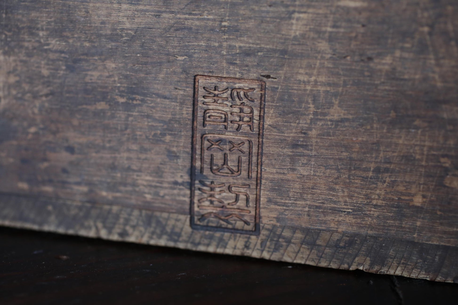 a close-up view of a wooden surface with a vertical, rectangular symbol or text carved into it.