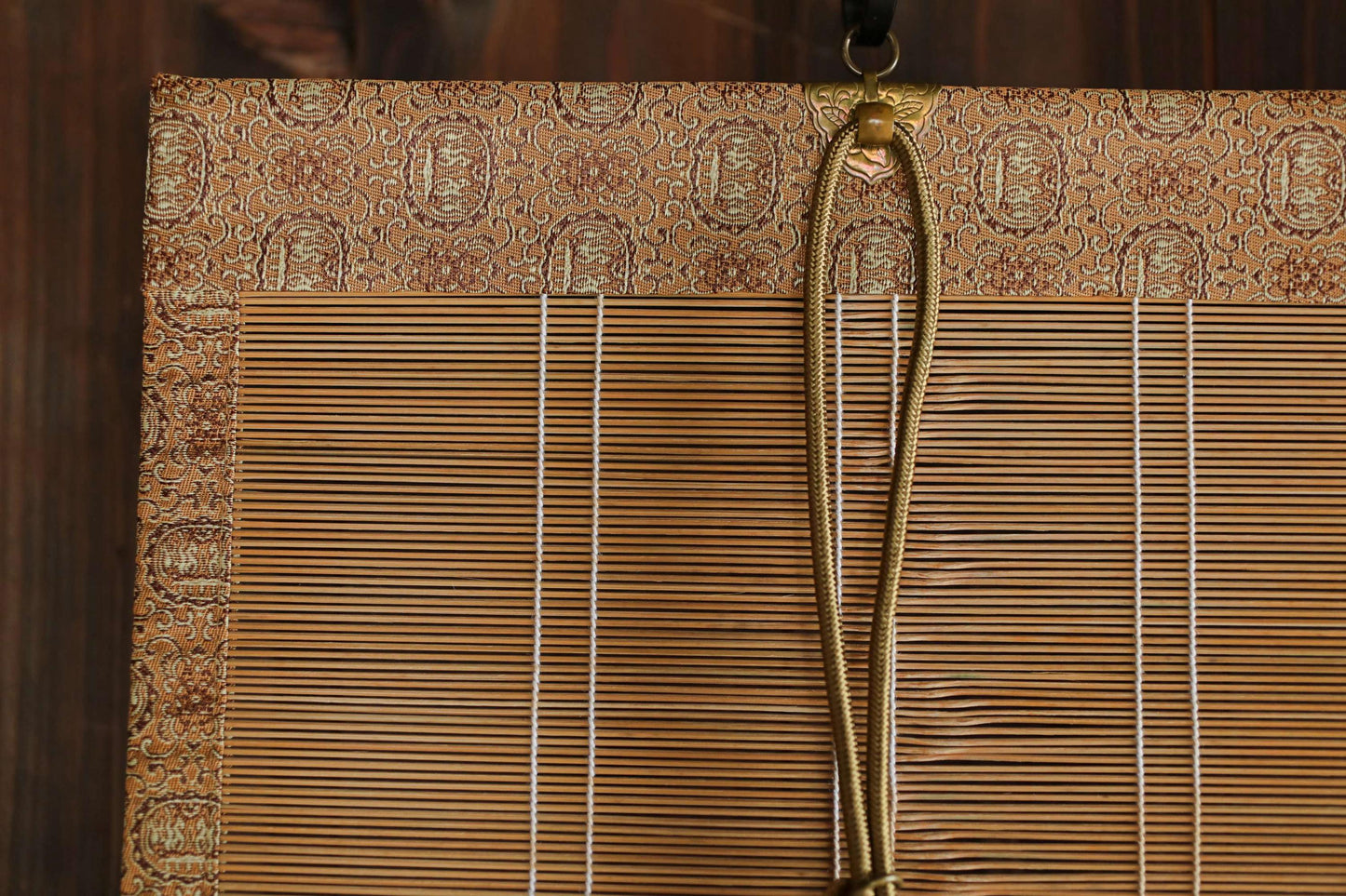 a close-up view of a bamboo blind with a gold rope hanging from it.