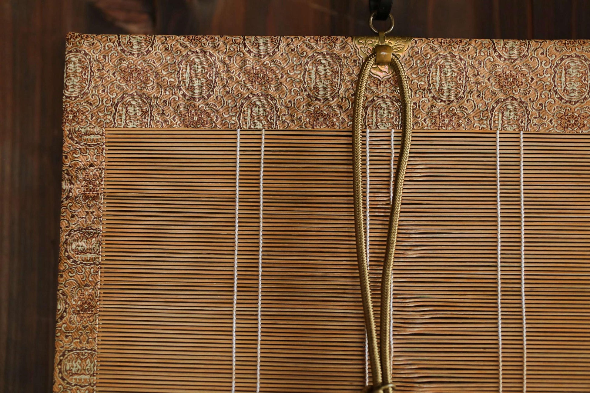 a close-up view of a bamboo blind with a gold rope hanging from it.