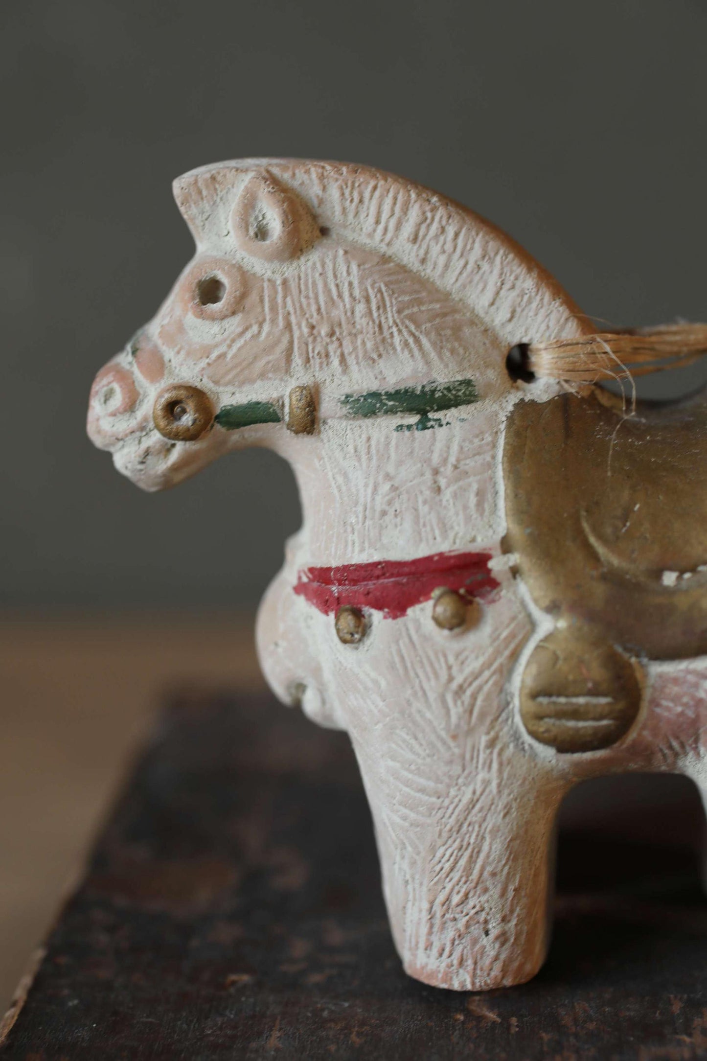 A white ceramic horse figurine with a red band around its neck and a brass saddle, sitting on a wooden surface.