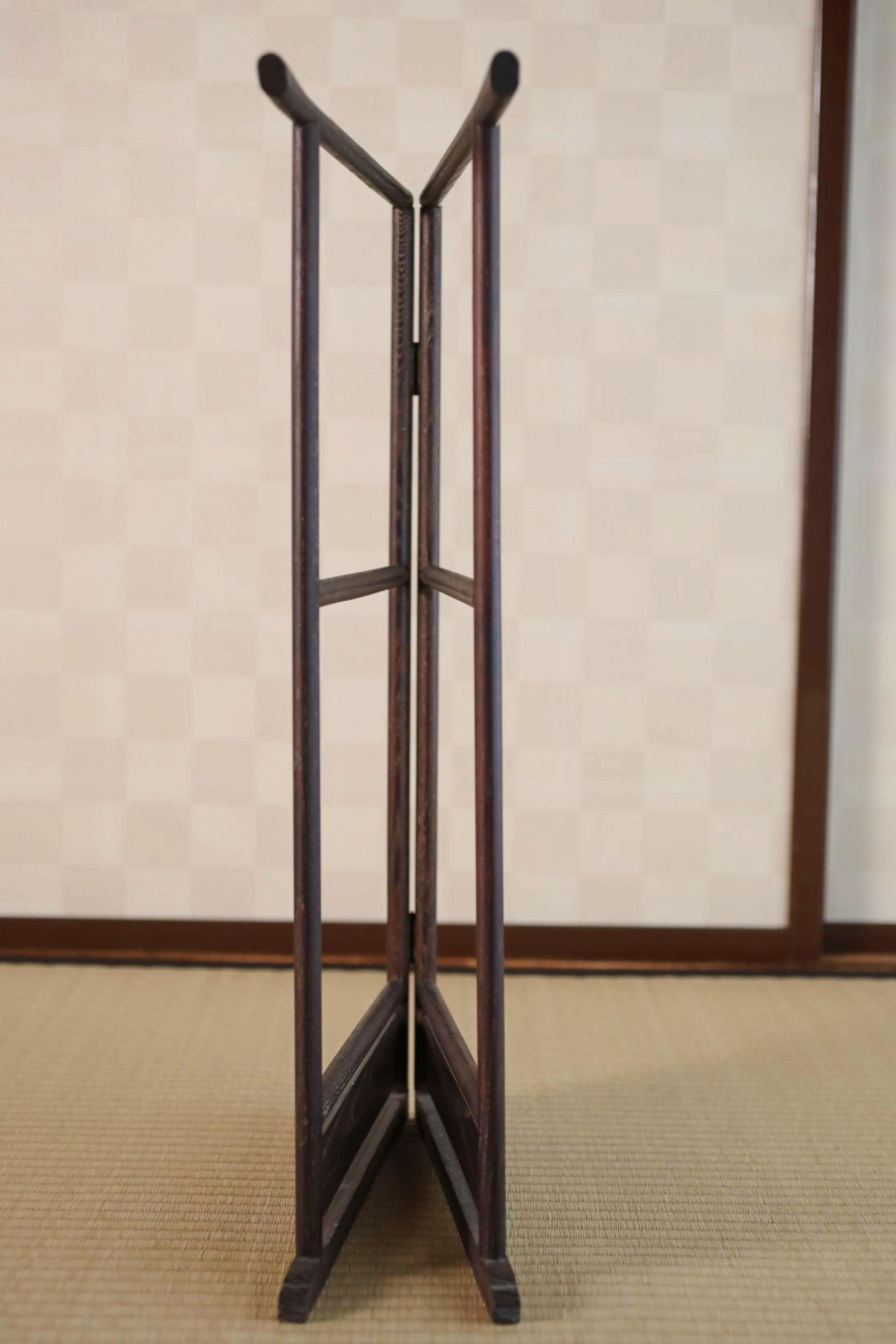 A wooden folding screen with two vertical bars on either side, standing upright on a beige mat.