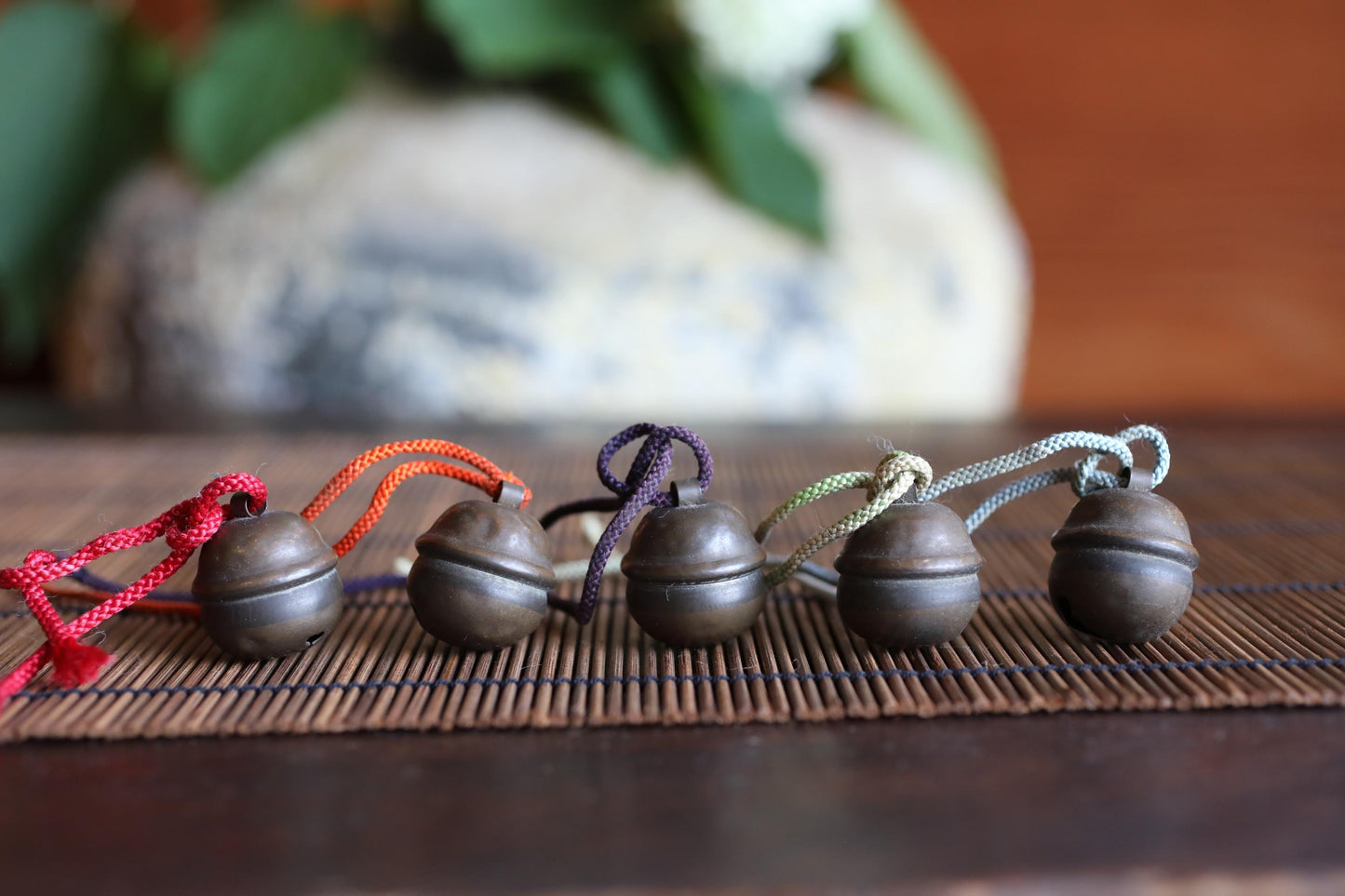 A row of five small, round metal bells with colorful strings attached, arranged on a wooden surface.