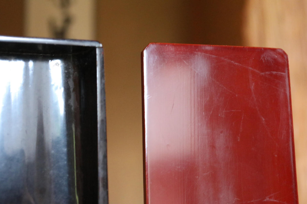 a close-up view of a red object, possibly a piece of furniture or a decorative item, next to a black object, possibly a metal or plastic item. The red object appears to be shiny and well-maintained, while the black object has some scratches and marks on it. The background is blurred, making the red object the main focus of the image.