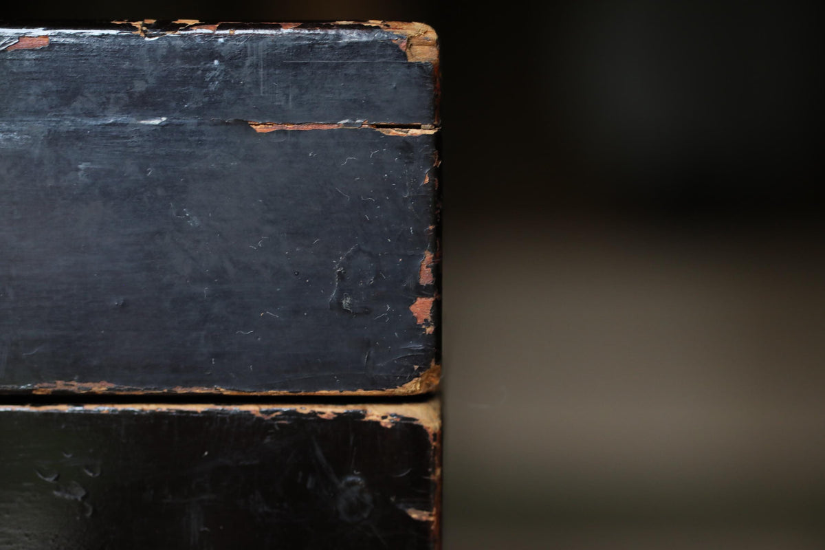 A close-up view of a weathered, black surface with visible signs of age and wear, including peeling paint and cracks.