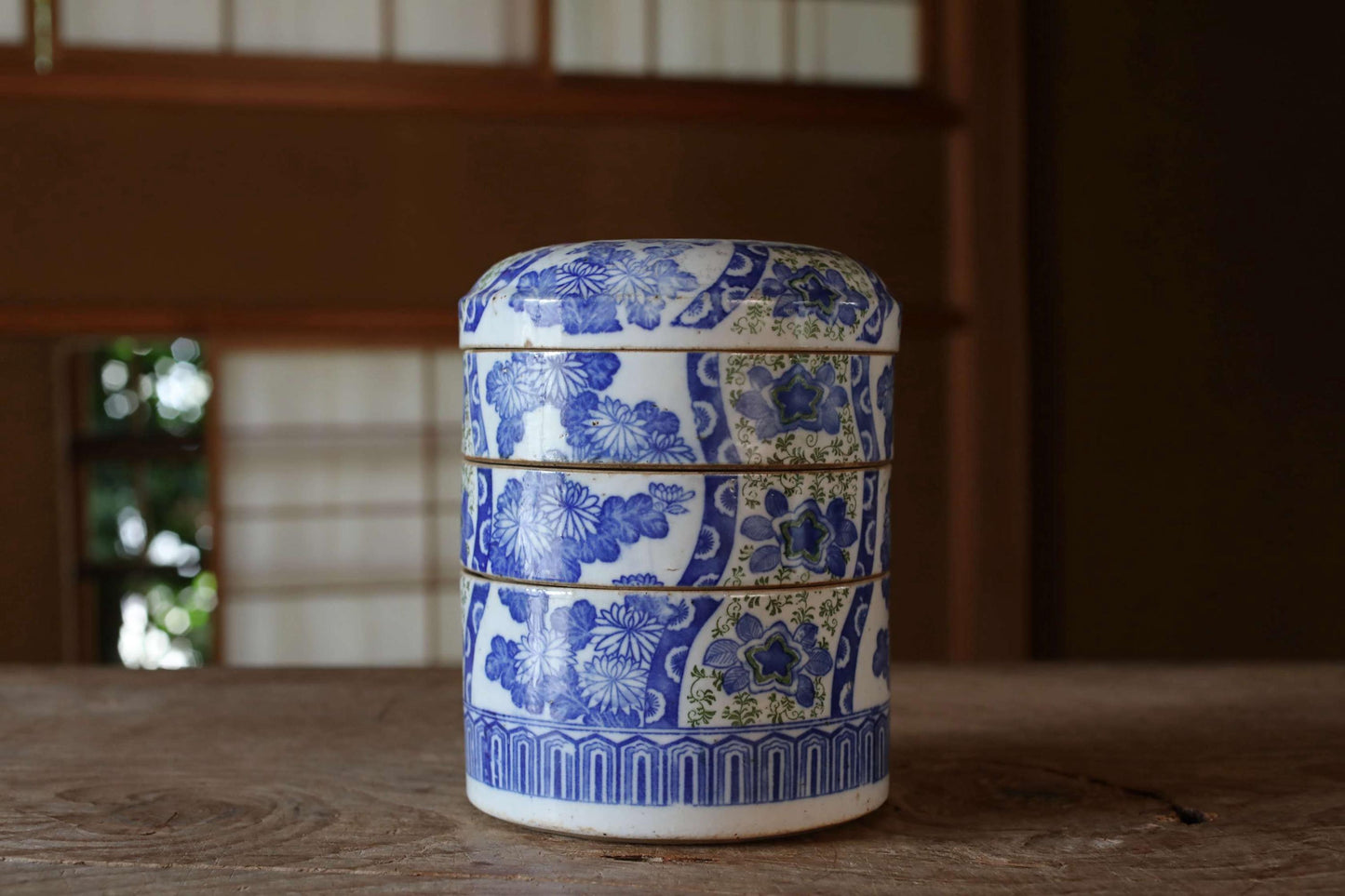 A ceramic container with a blue and white floral pattern, featuring three stacked layers, sits on a wooden surface.