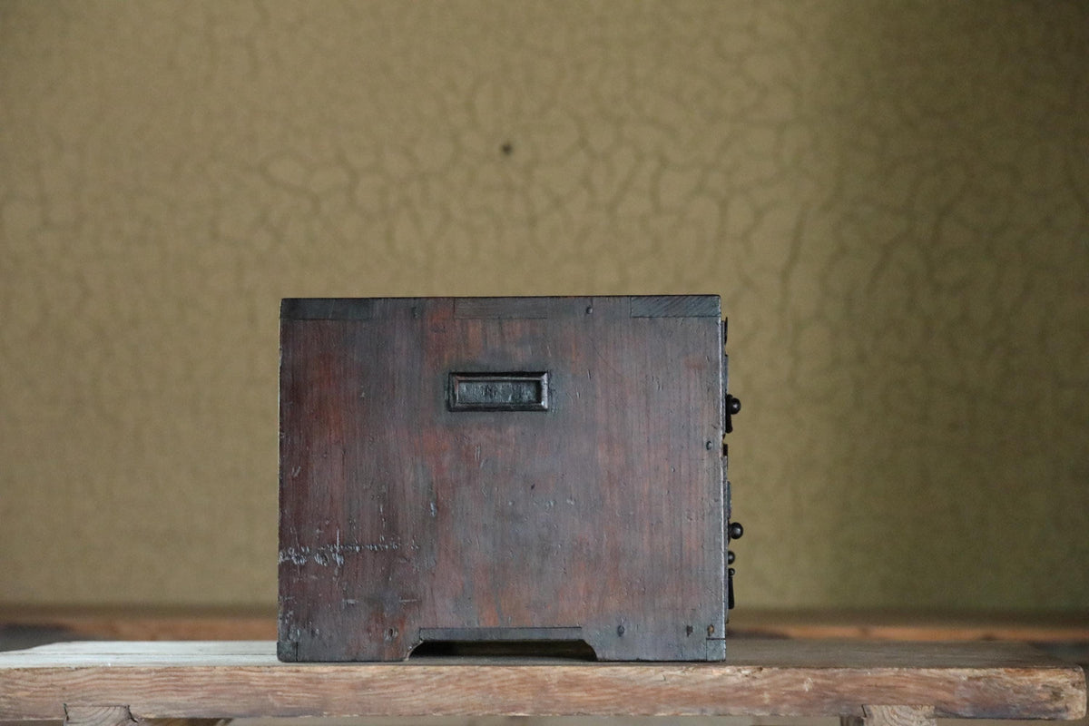 A wooden box with a metal handle sits on a wooden surface against a textured green background.