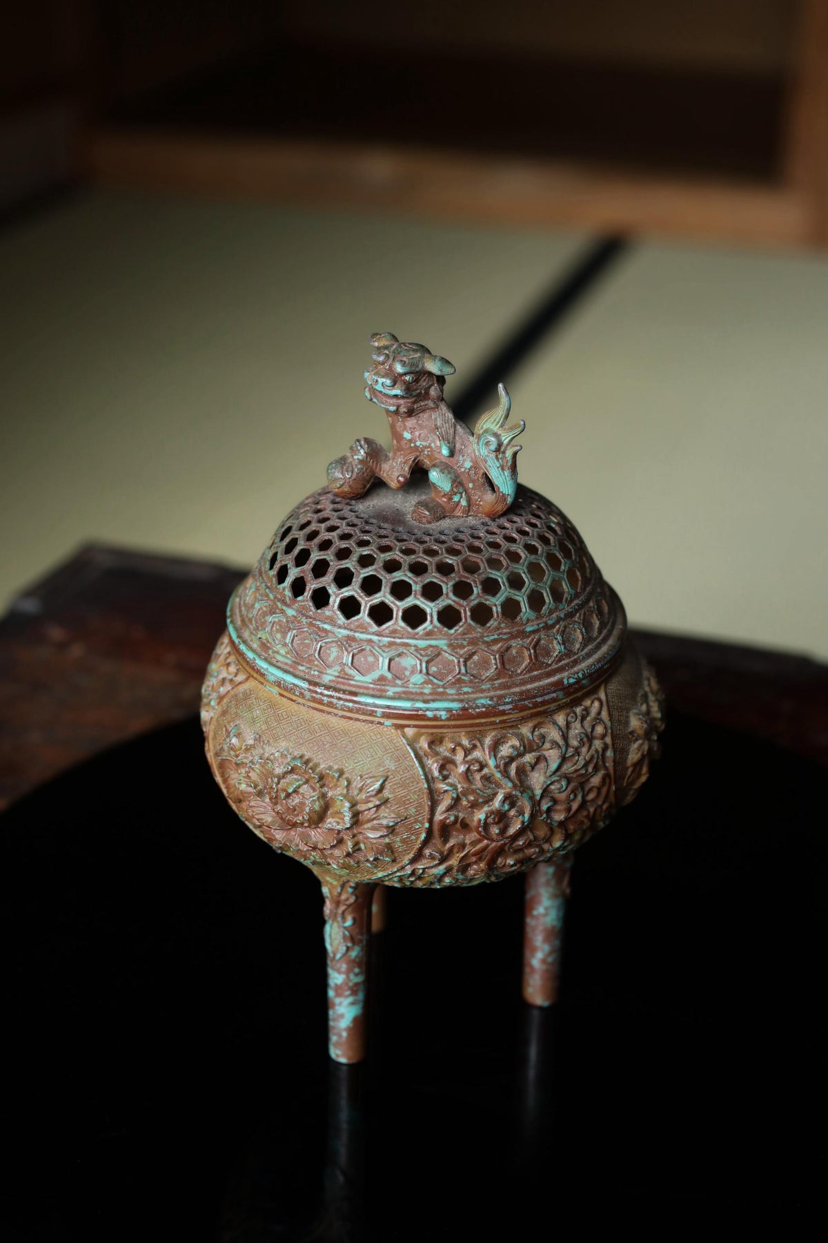 An ornate bronze incense burner with a dragon figure on top, sitting on a wooden surface.