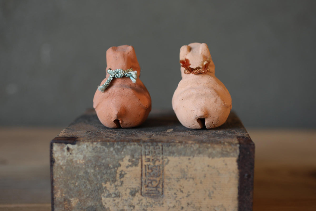 Two small clay figurines, one brown and one pink, are sitting on a wooden surface.