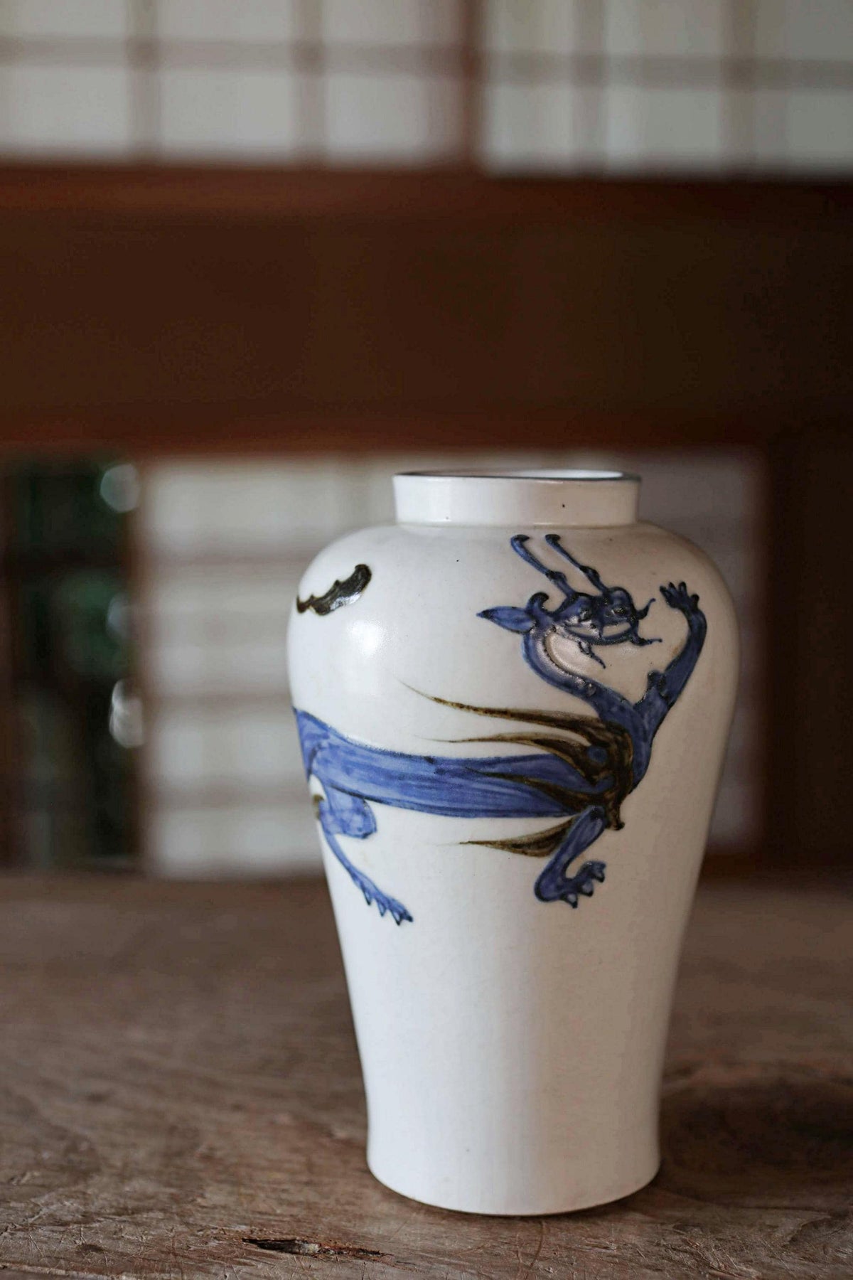 A white ceramic vase with a blue dragon design on it, sitting on a wooden surface.