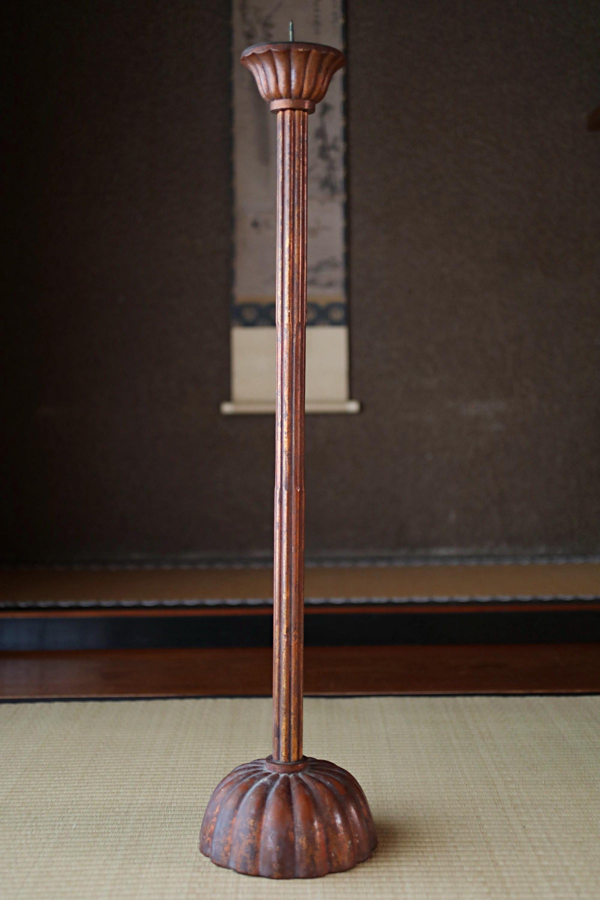 a tall, ornate candle holder with a fluted design, standing on a beige mat.