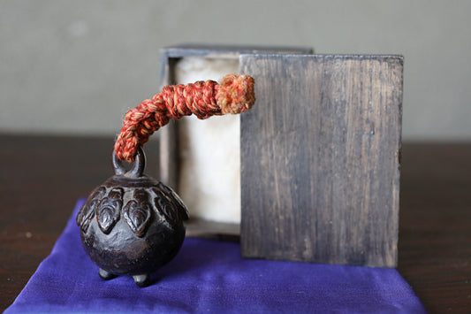 A small, ornate metal object with a red and orange rope wrapped around it, placed on a purple cloth.