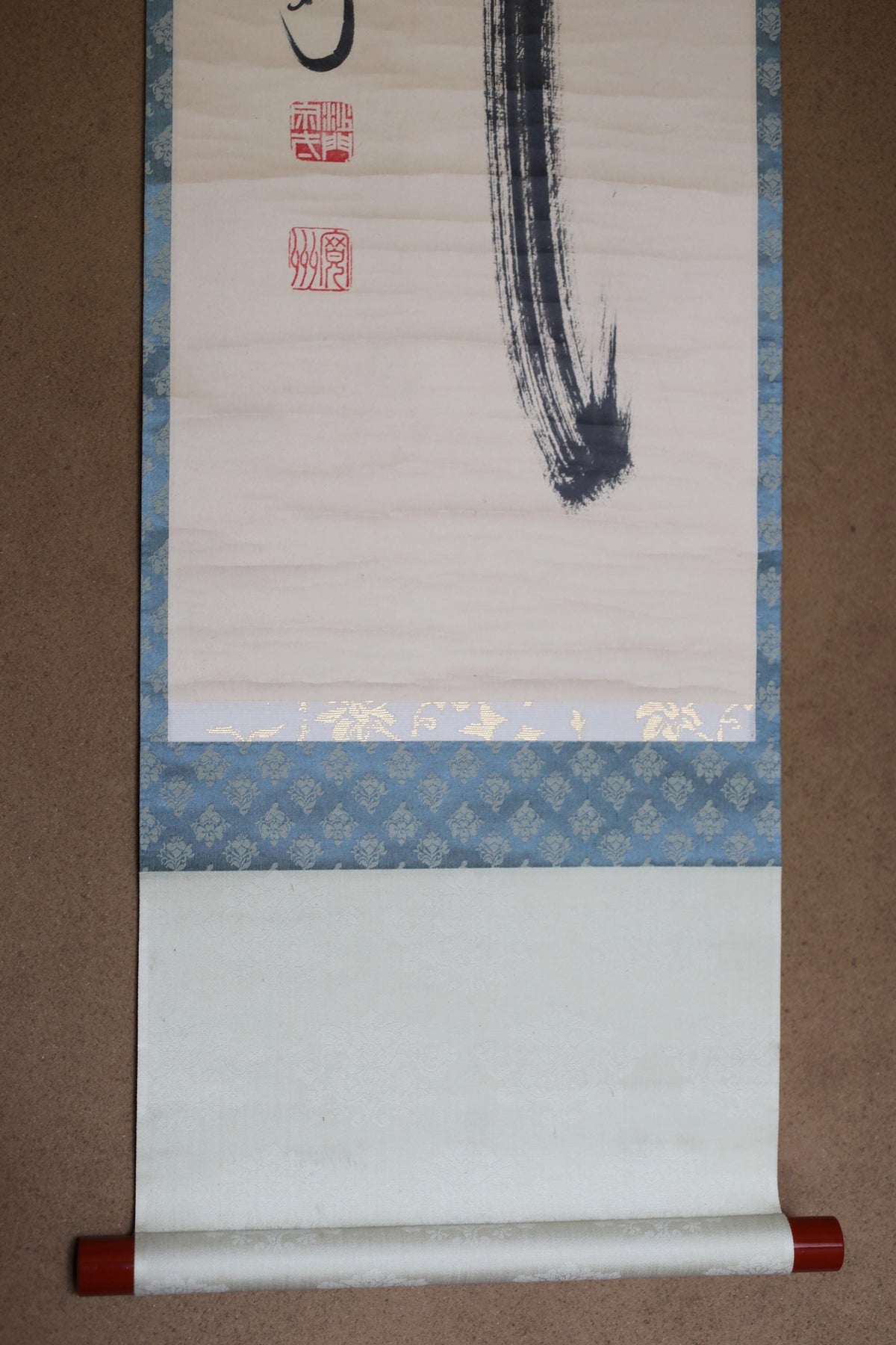 a roll of paper with a black brush stroke on it, and there is a blue and white patterned fabric below it.