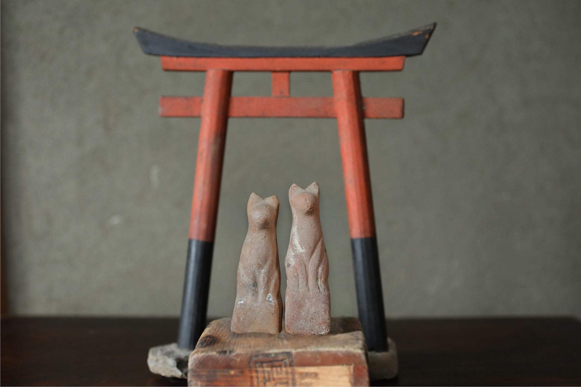 two small statues of cats, one on each side of a red and black torii gate, which is a traditional Japanese gate used at the entrance to a Shinto shrine.