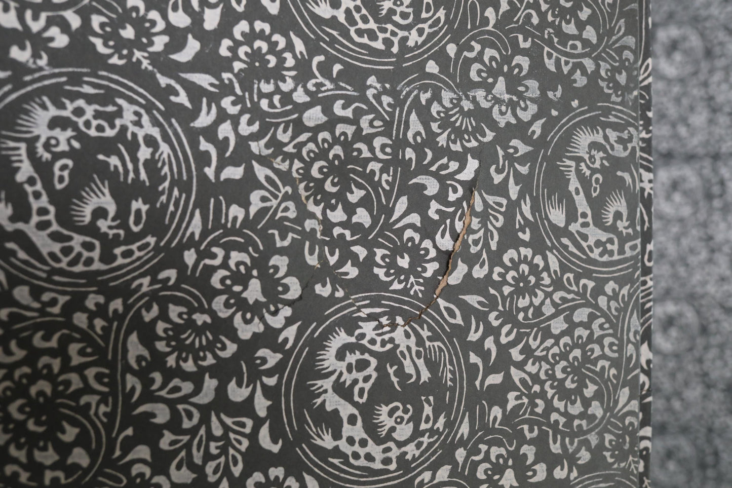 a close-up view of a wall with a repeating pattern of black and white floral designs. The pattern is intricate and detailed, with a few small cracks visible on the surface.