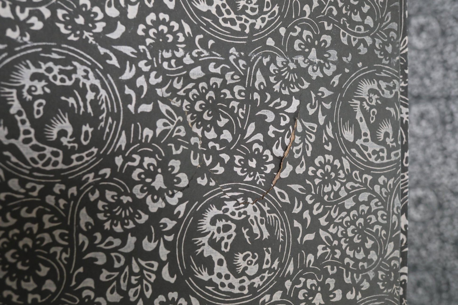 a close-up view of a wall with a repeating pattern of black and white floral designs. The pattern is intricate and detailed, with a few small cracks visible on the surface.