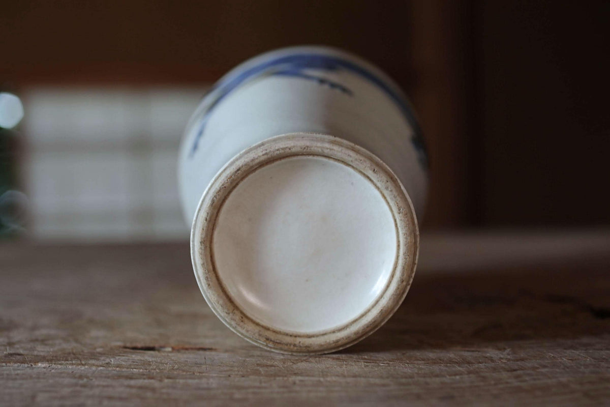 A white ceramic vase with blue designs on its surface, placed on a wooden surface.