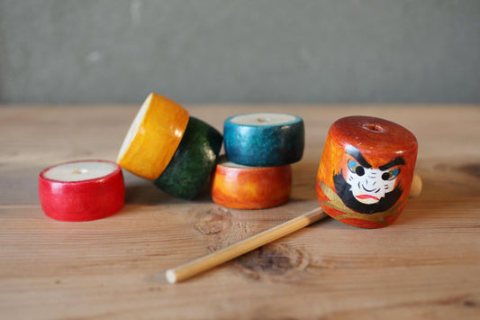 A collection of colorful wooden objects, including a wooden doll with a face, a wooden stick, and other wooden items, are arranged on a wooden surface.