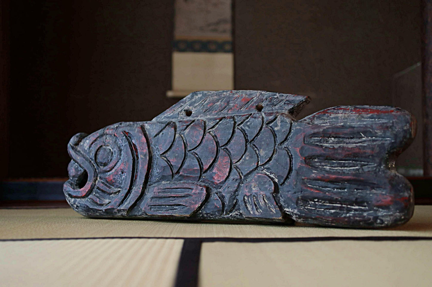 A wooden fish sculpture with intricate carvings and red accents is displayed on a wooden surface.