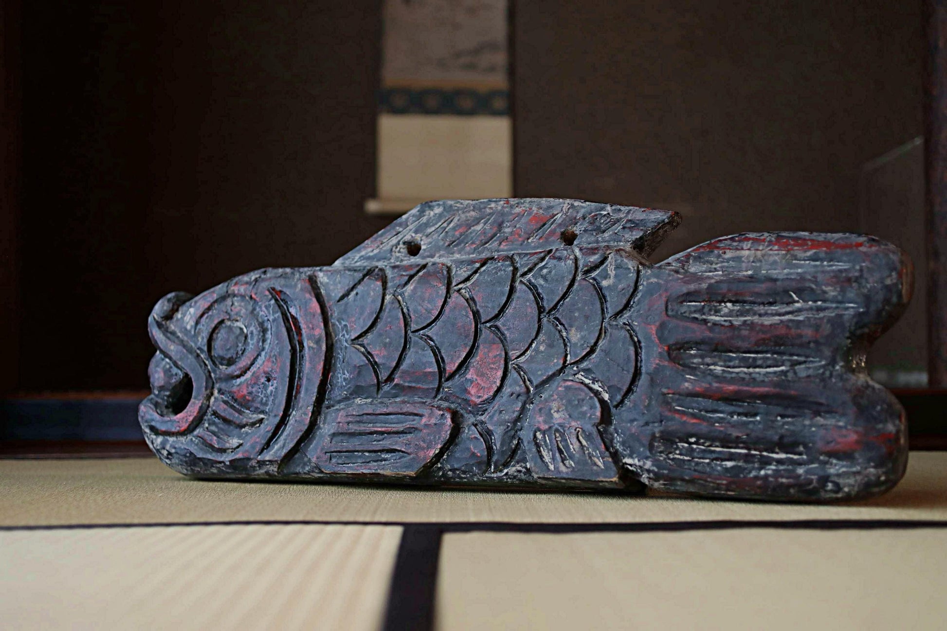 A wooden fish sculpture with intricate carvings and red accents is displayed on a wooden surface.