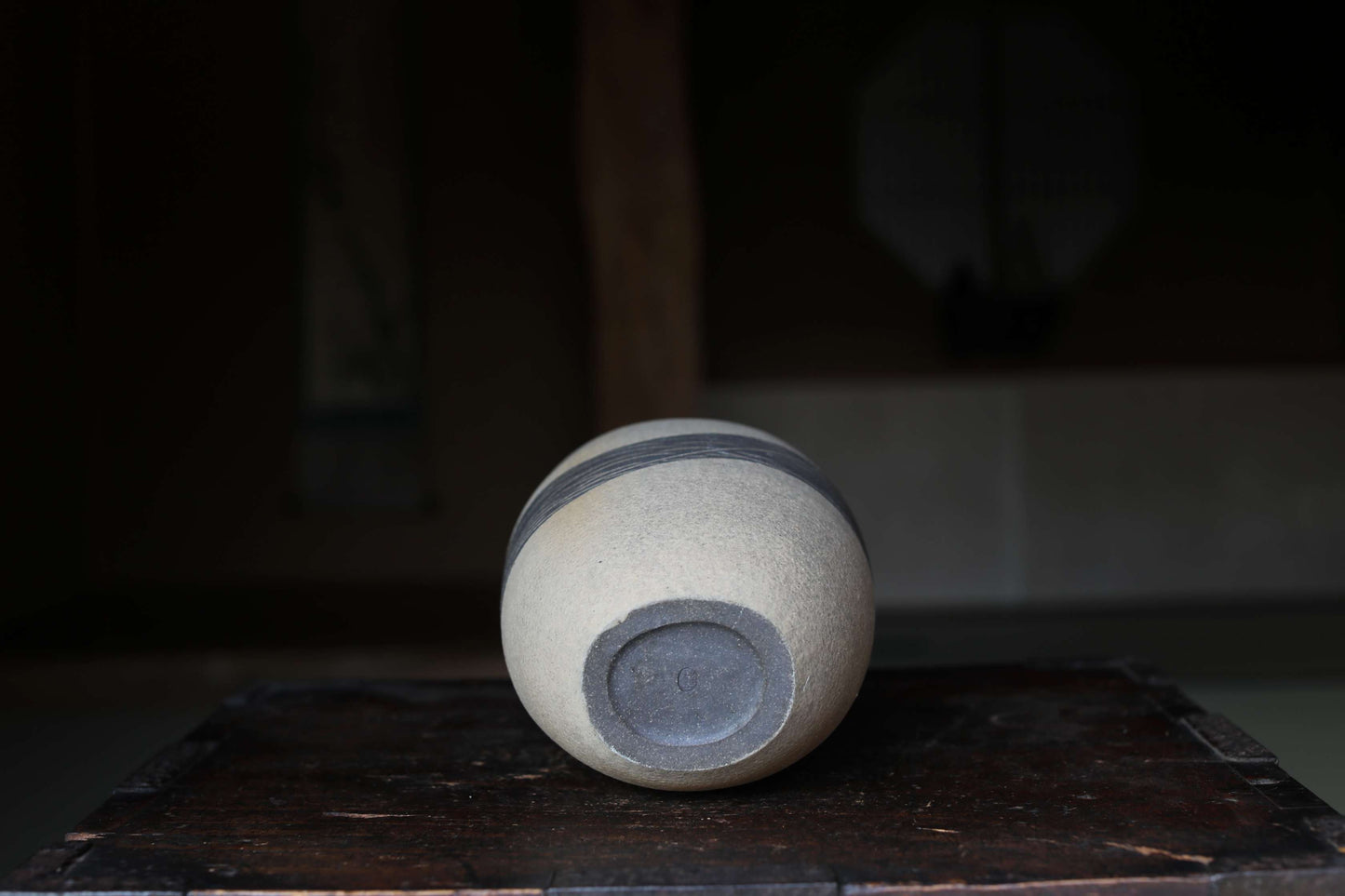 A white ceramic vase with a black stripe on the side is placed on a wooden surface.