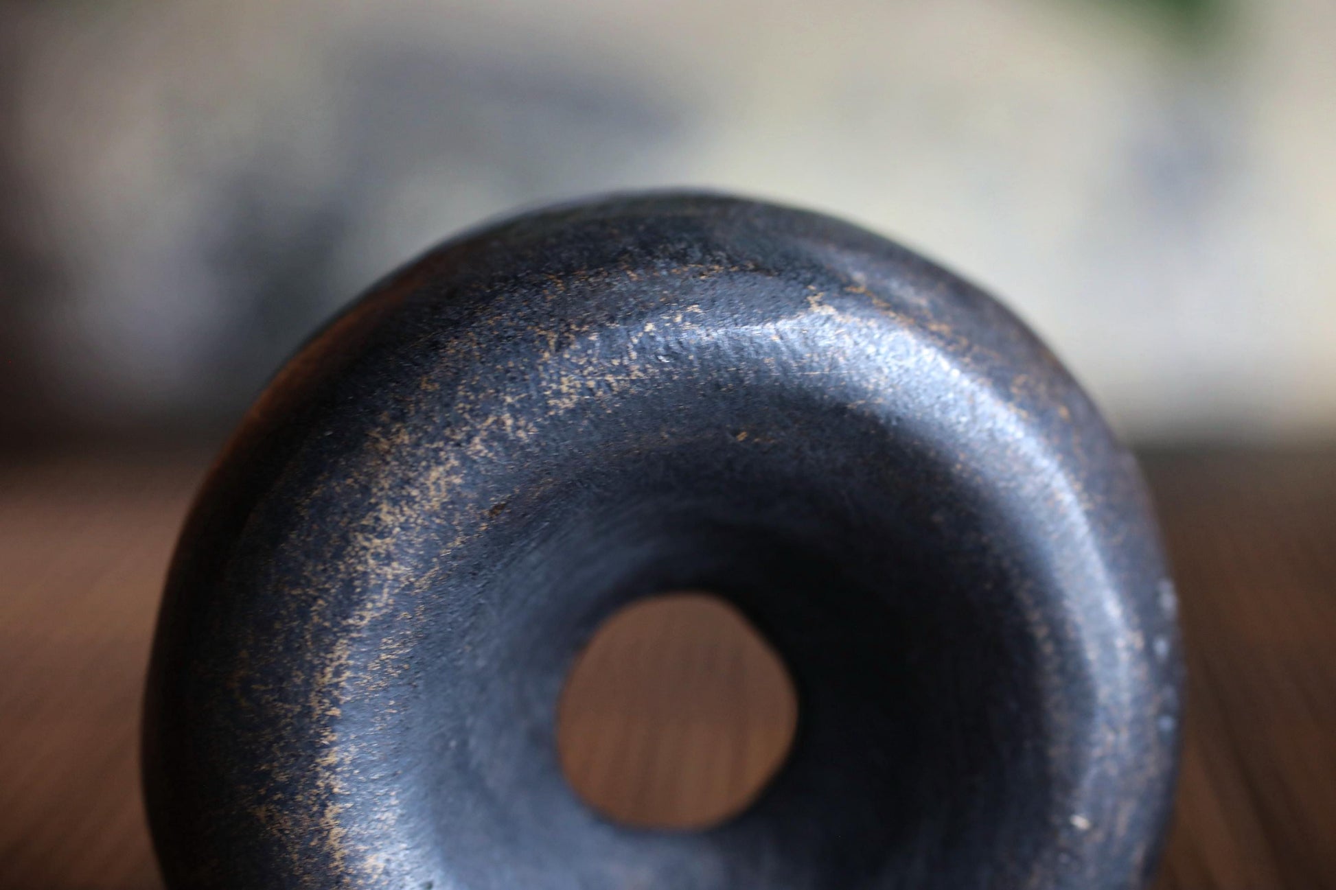 A close-up view of a dark, textured object with a hole in the center, possibly a ceramic or metal piece.