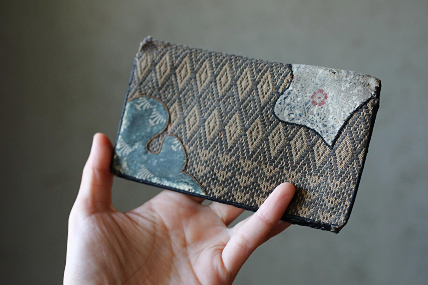 A hand holding a wallet with a patterned design.