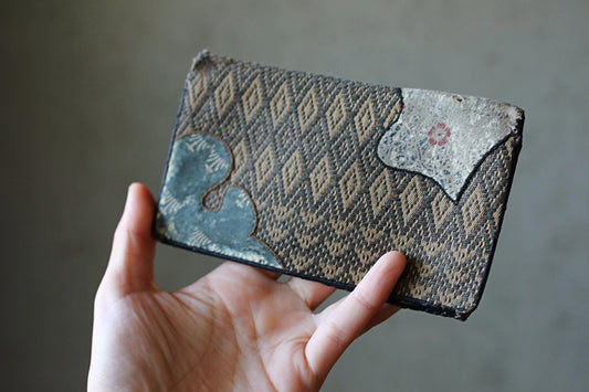 A hand holding a wallet with a patterned design.