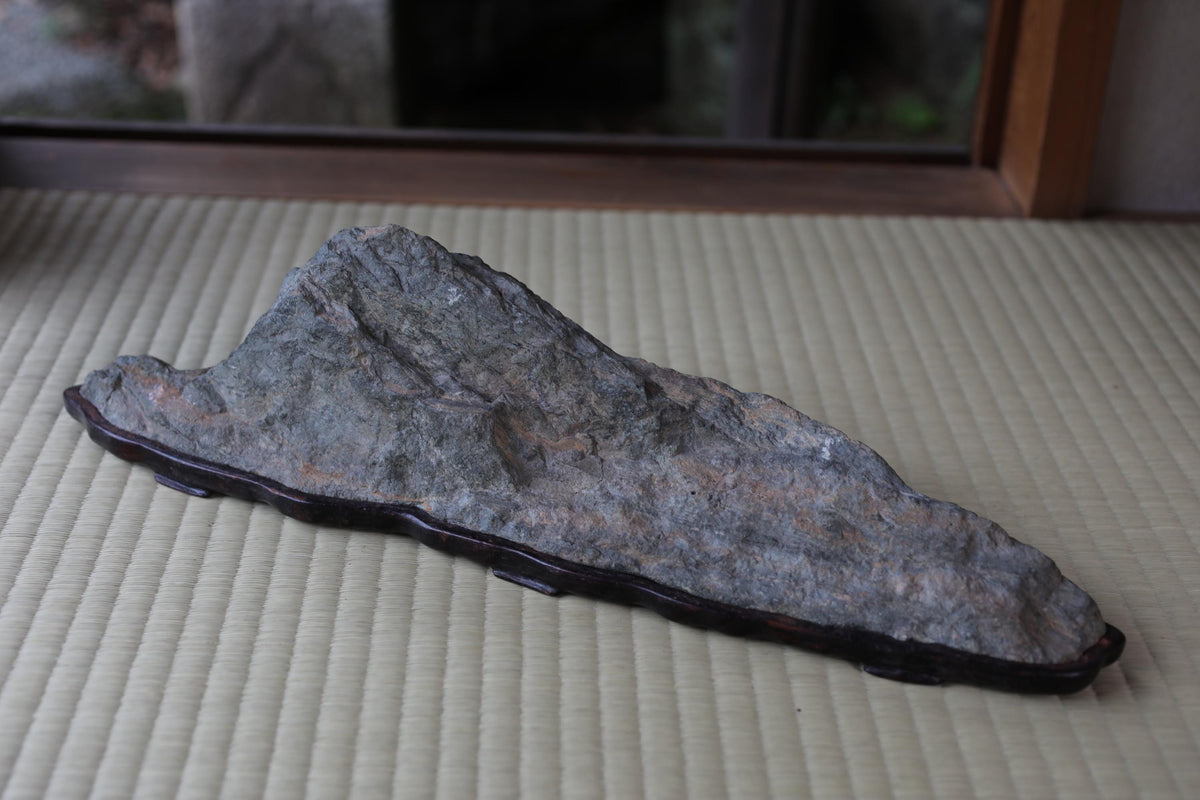 a large, gray rock with a dark border, resting on a woven mat or mat-like surface.