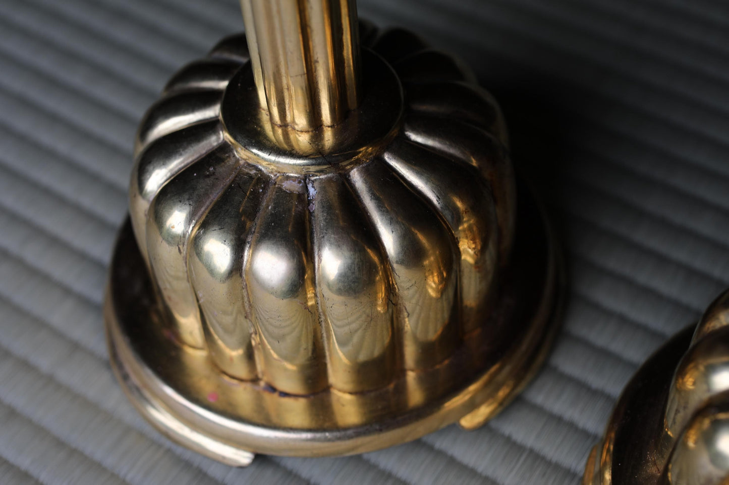 A close-up view of a shiny, golden-colored metal object, possibly a candlestick or a decorative piece, resting on a textured surface.