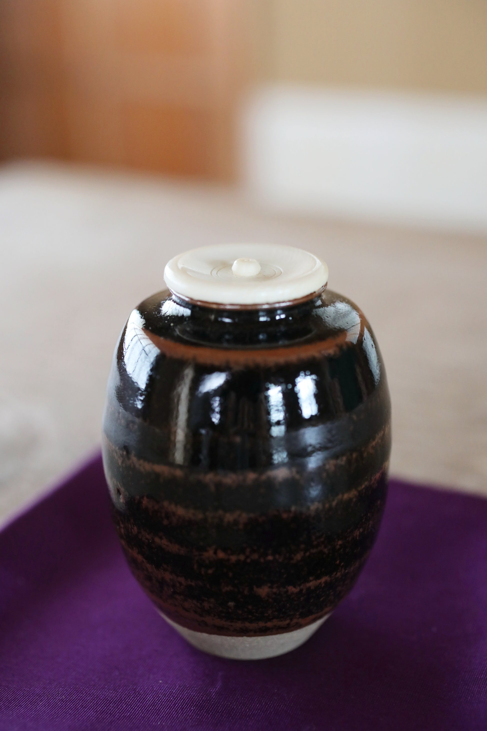 A black and brown ceramic jar with a white lid sits on a purple surface.