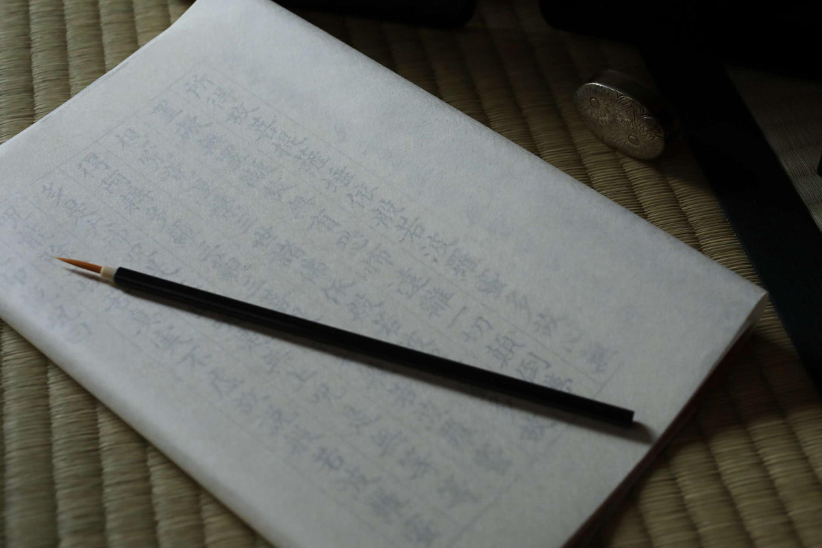 a piece of paper with Japanese characters on it, along with a black pencil resting on top of the paper.