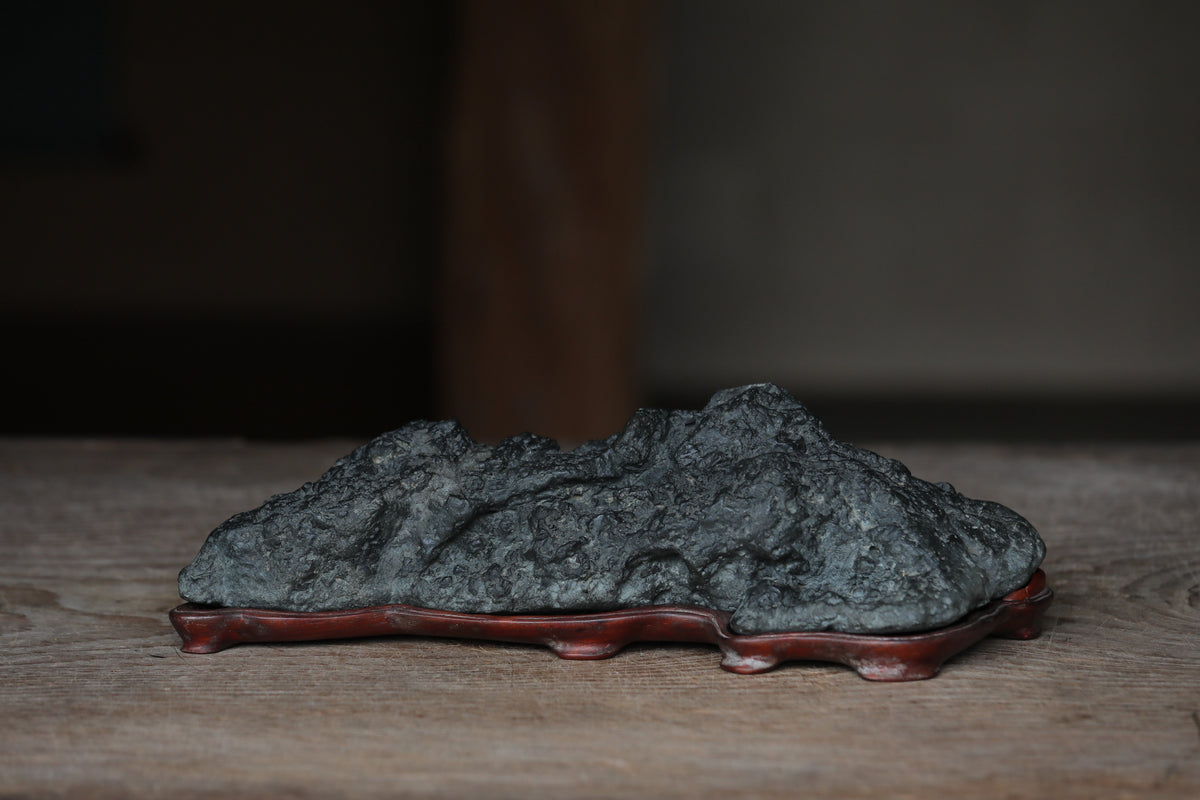 A dark gray rock formation sits on a red base, placed on a wooden surface.