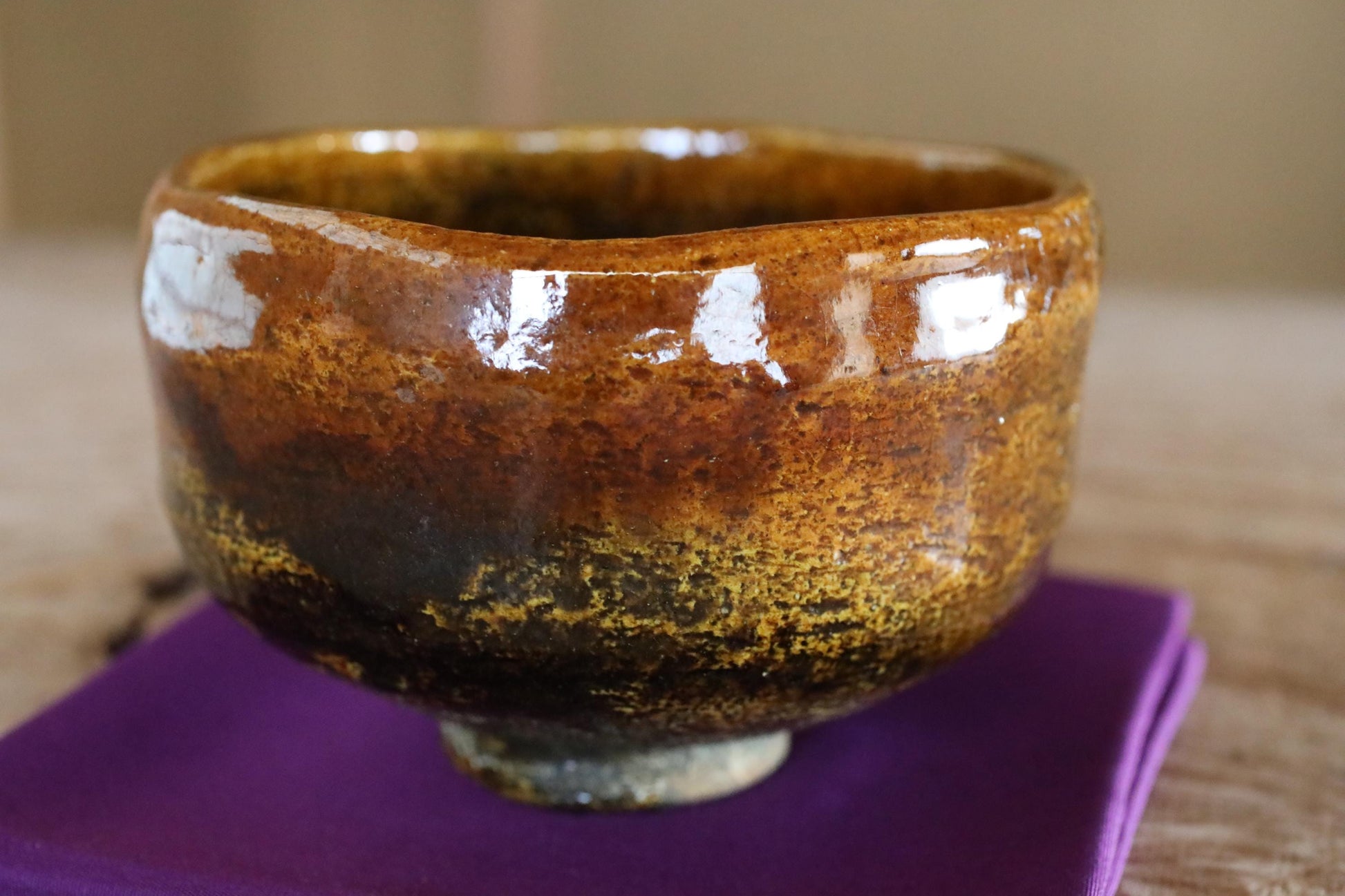 A close-up image of a brown ceramic bowl with a textured surface, resting on a purple cloth.