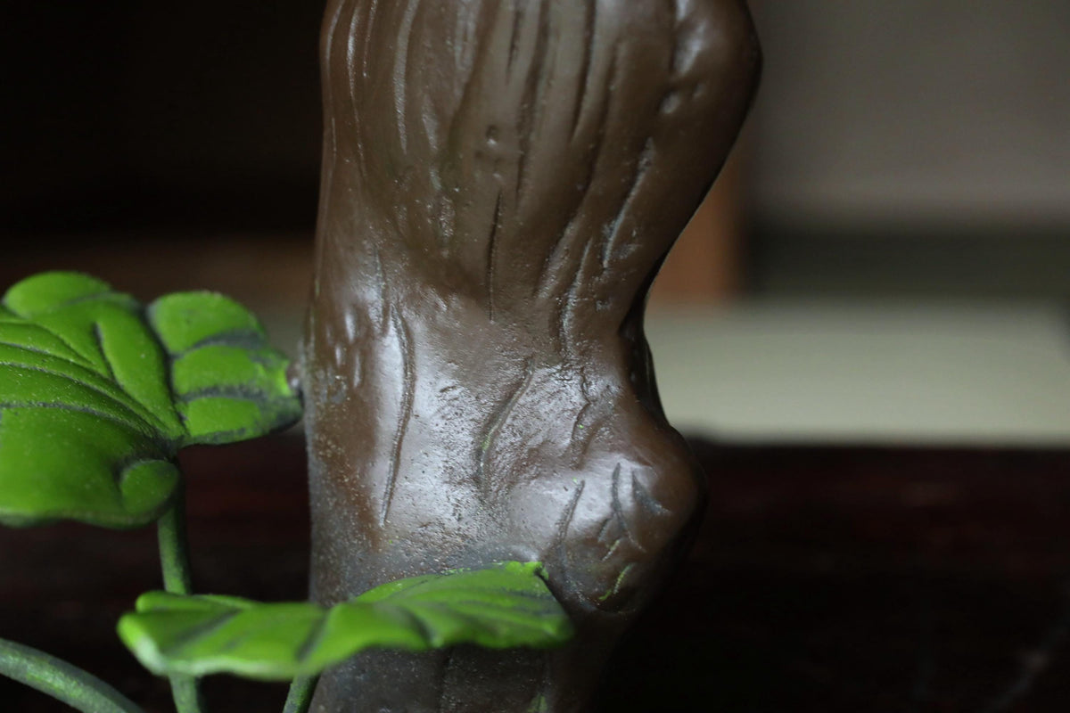 A close-up view of a brown, textured object resembling a tree trunk or branch, with green leaves attached to it.