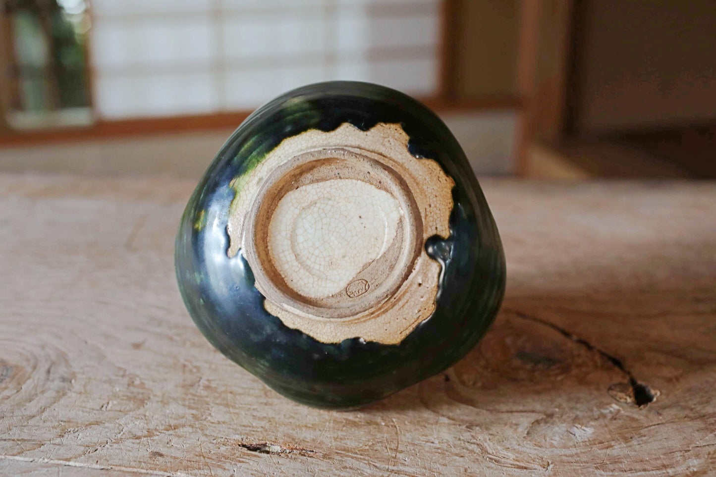 A ceramic vase with a green and black color scheme sits on a wooden surface.