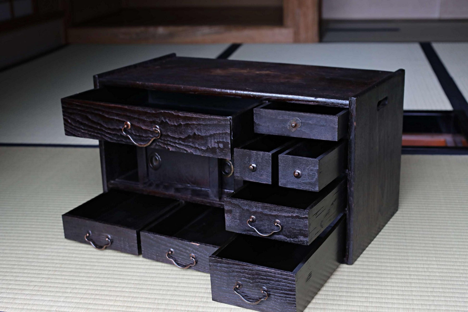 A dark wooden cabinet with multiple drawers, sitting on a tatami mat.