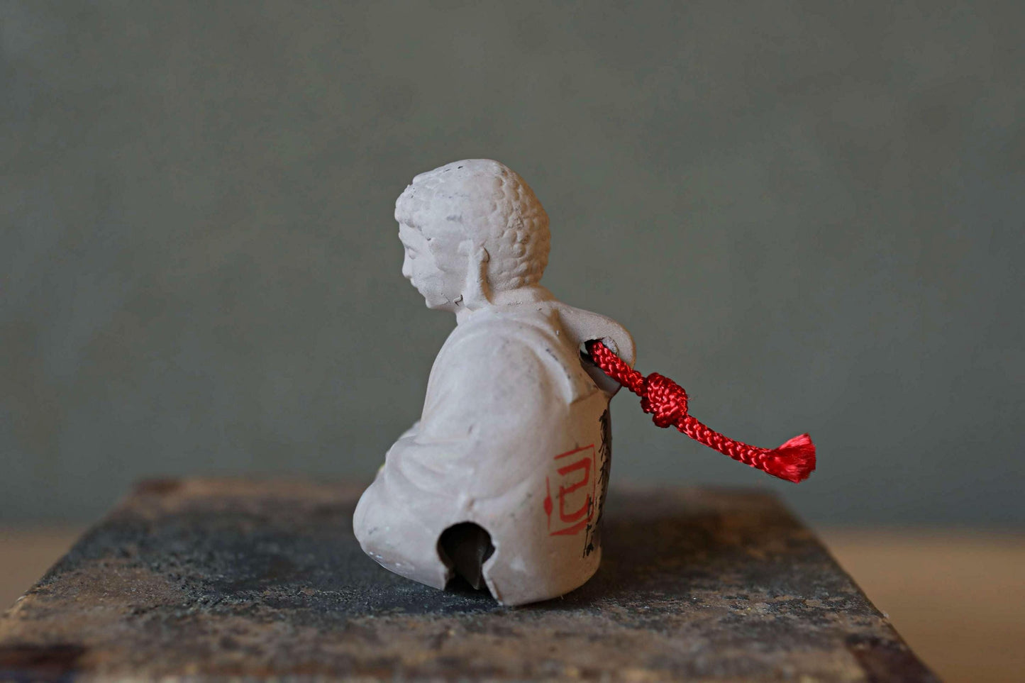 A small white figurine with a red string attached to it, sitting on a gray surface.